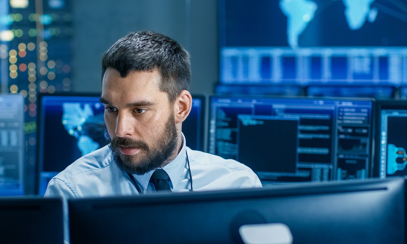 In the System Control Center Operator Working Surrounded by Displays Showing Relevant Data. In the Background Data with Interactive Map.