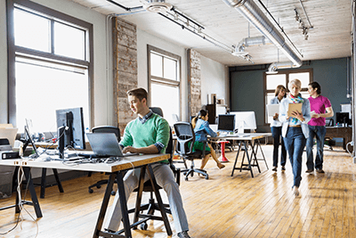 Photo of open floor plan office setting with people using technology.